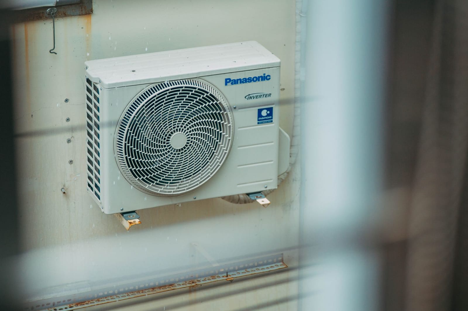 An air-to-air heat pump outdoor unit mounted on a house wall beside a window